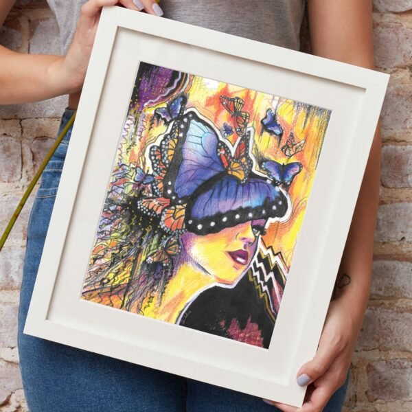 Person holding a framed artwork with a colorful butterfly design against a brick wall.